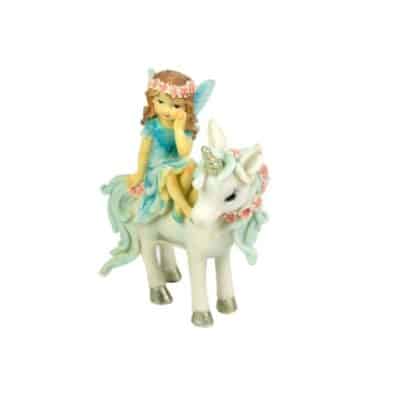A figurine depicting a young girl with fairy wings sitting atop a unicorn adorned with a floral wreath around its neck. Both the girl and the unicorn feature pastel colors, with the girl in a sparkling blue dress and the unicorn in shades of white and light blue.