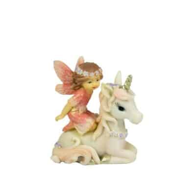 A figurine of a fairy with pink wings sitting on a white unicorn with a purple floral necklace on a plain background.