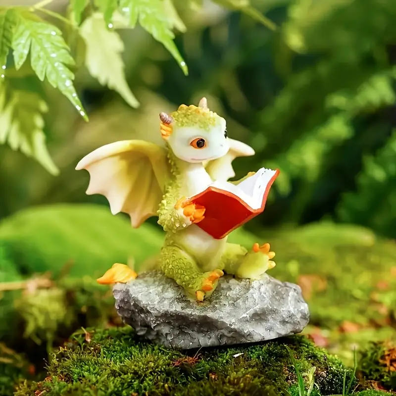 A cute dragon figurine with green scales and tiny wings sitting on a rock, engrossed in reading a red book amidst a lush, green background.