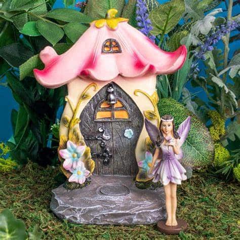 Mini fairy garden scene with a fairy house and fairy figure on moss with plants and flowers.